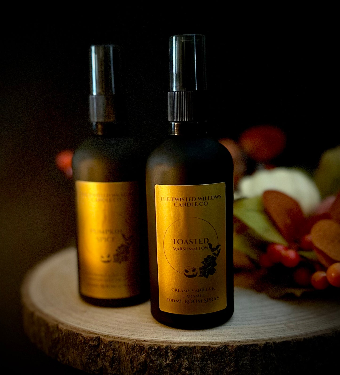 Dark autumn scene with a matte black Toasted Marshmallow room spray beside dried herbs