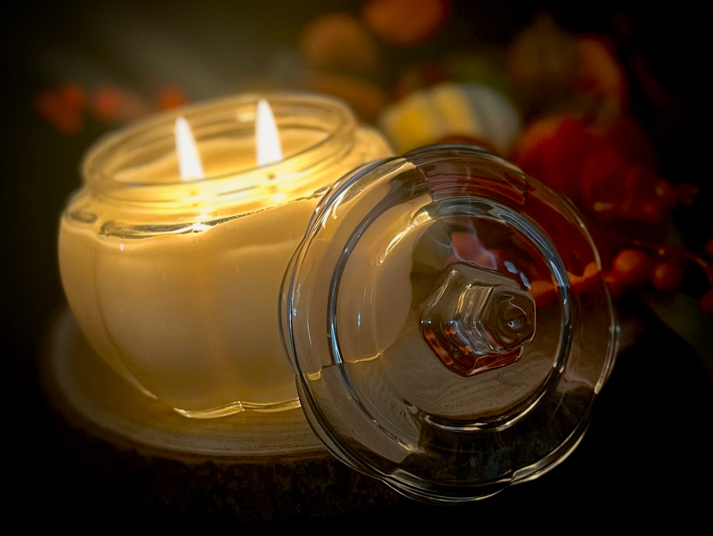A haunting autumn scene with a glowing pumpkin spice candle beside dried foliage.