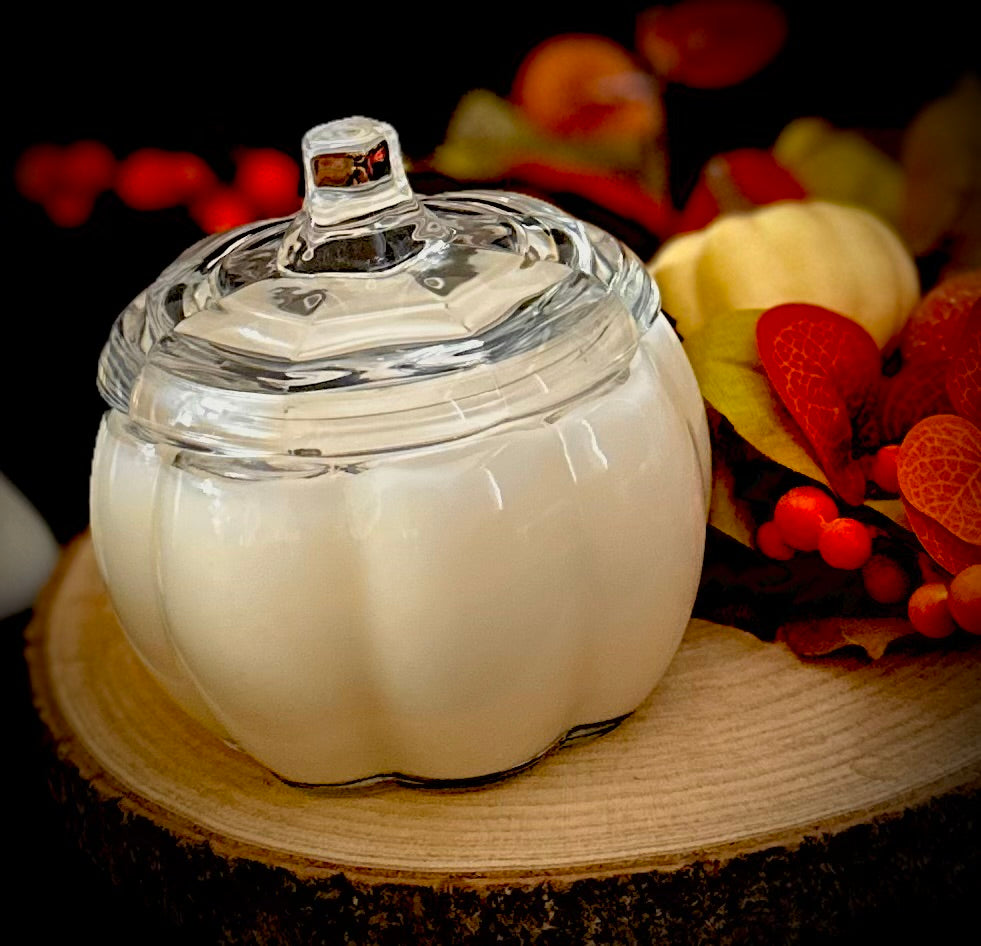A large clear glass pumpkin jar candle on an autumn floral display.