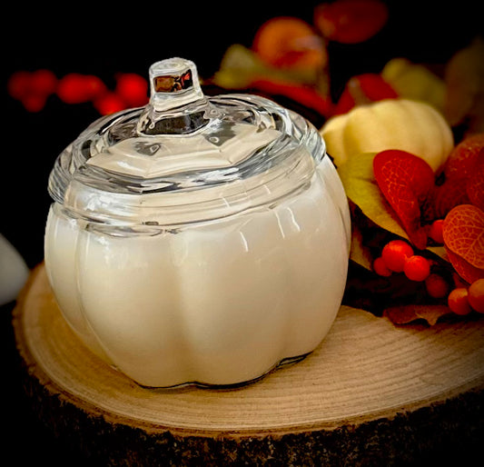 A large clear glass pumpkin jar candle on an autumn floral display.
